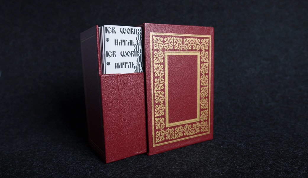 Red leather slipcase, partially open, revealing the stack of booklets inside.